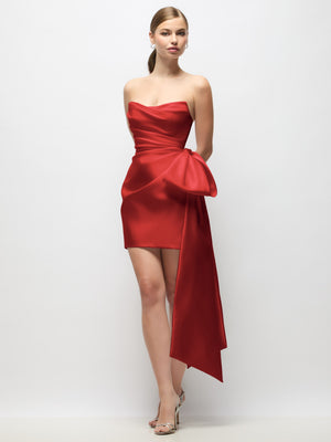 Red strapless satin mini dress with draped pleats and dramatic long bow tail