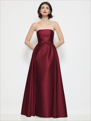 Cabernet red strapless satin column dress with bow waist and draped overskirt