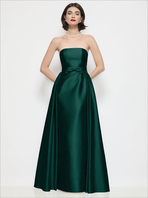 Strapless satin column dress in deep green with waist bow and draped overskirt