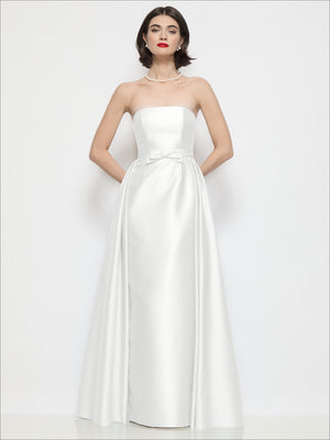 White satin strapless column dress with bow at waist and overskirt overlay