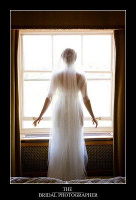 Bride with wedding veil standing by window 