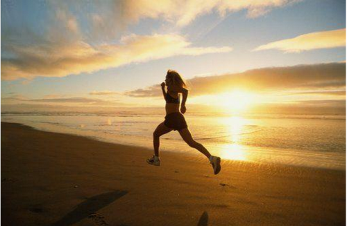 fitness woman running along beach in sunset